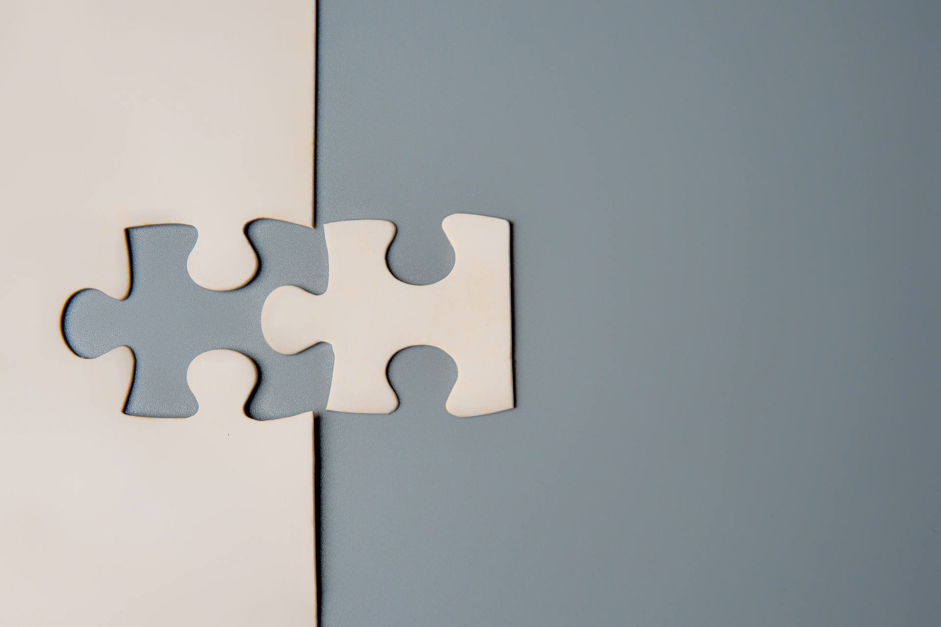 Two puzzle pieces connecting, one white and one grey, on a contrasting background.